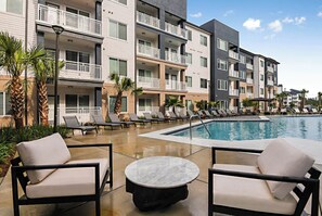 Un espace piscine d’hôtel avec des chaises longues et une table, entouré d’immeubles à plusieurs étages dotés de balcons.