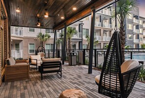 A covered outdoor area with seating, including a sofa and chairs, and a hanging chair. - Landing | Spectacular 1BD, Rooftop Lounge (Bellview)