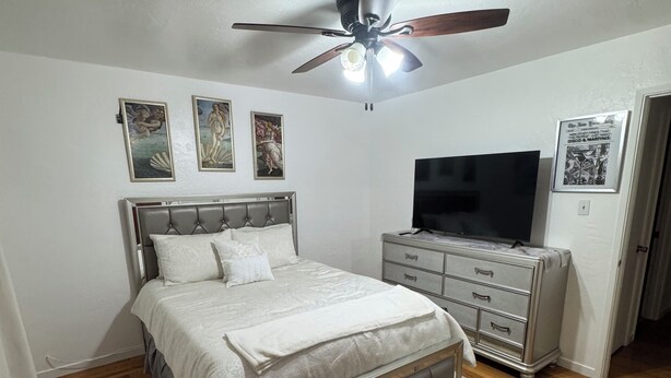 Ein Schlafzimmer mit einem Bett, einem Deckenventilator, einem Fernseher, einem Schminktisch und Kunstwerken an den Wänden.