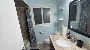 Ein Badezimmer mit einem weißen Waschbecken, einem Spiegel, einem Fenster und einer Duschkabine.