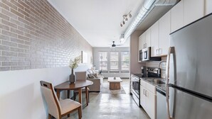 A modern kitchen with a brick wall, a dining area with a table and chairs, and a large refrigerator. - Landing | Beautiful 1BD, Pool, Game Room (Bellview)