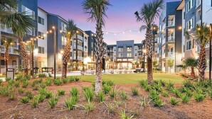A modern hotel with multiple floors, outdoor seating areas, and palm trees. - Landing | Beautiful 2BD, Game Room, Yoga Studio (Bellview)