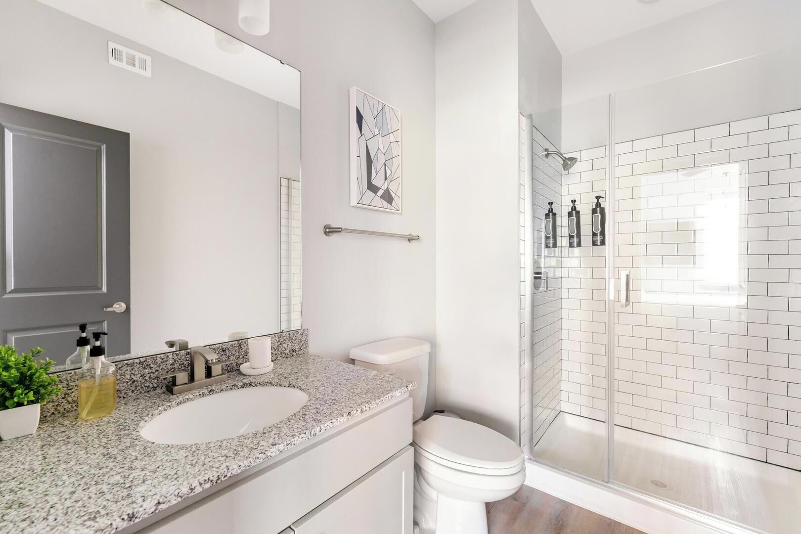 A modern bathroom with a granite countertop, white fixtures, a glass shower enclosure, and a door with a handle.