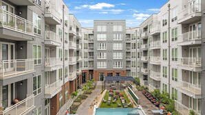 Un immeuble résidentiel à plusieurs étages doté de balcons, d’une cour intérieure avec une piscine et d’un espace extérieur aménagé pour s’asseoir.