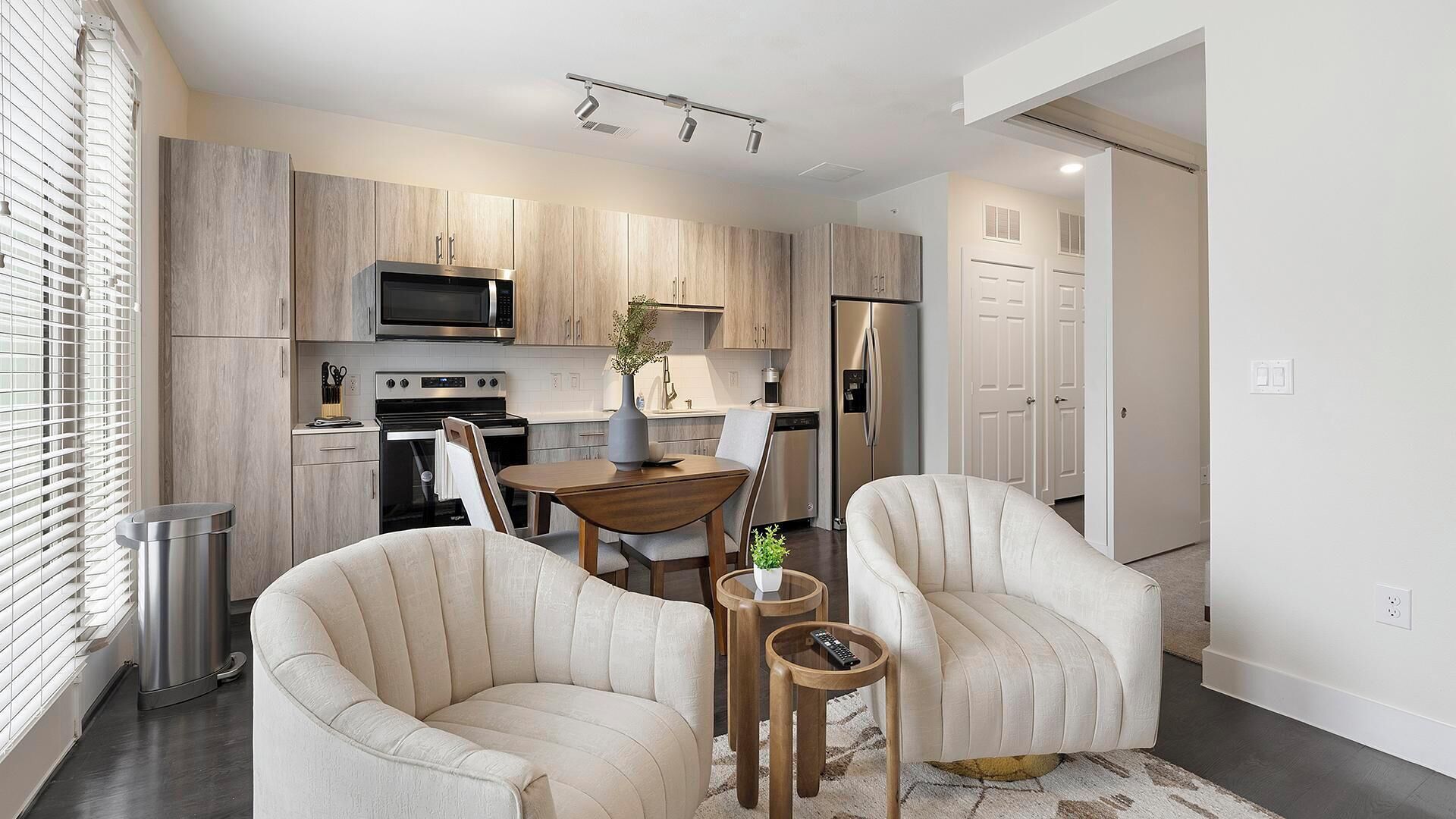A modern kitchen with built-in appliances, a dining area with a table and chairs, and a living space with two armchairs.