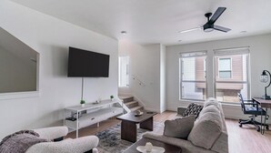 Een moderne woonkamer met een flatscreen televisie, een bank, een salontafel en een trap naar een buitenruimte.