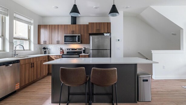 Een moderne keuken met houten kastjes, roestvrijstalen apparatuur en een centraal eiland met barstoelen.