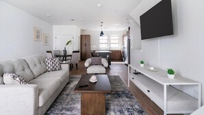 Een moderne woonkamer met een bank, salontafel, televisie, en een eethoek op de achtergrond.