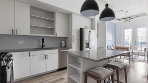 Una cucina moderna con mobili chiari in legno, un'isola centrale con sgabelli da bar, un forno integrato e una macchina per il caffè.