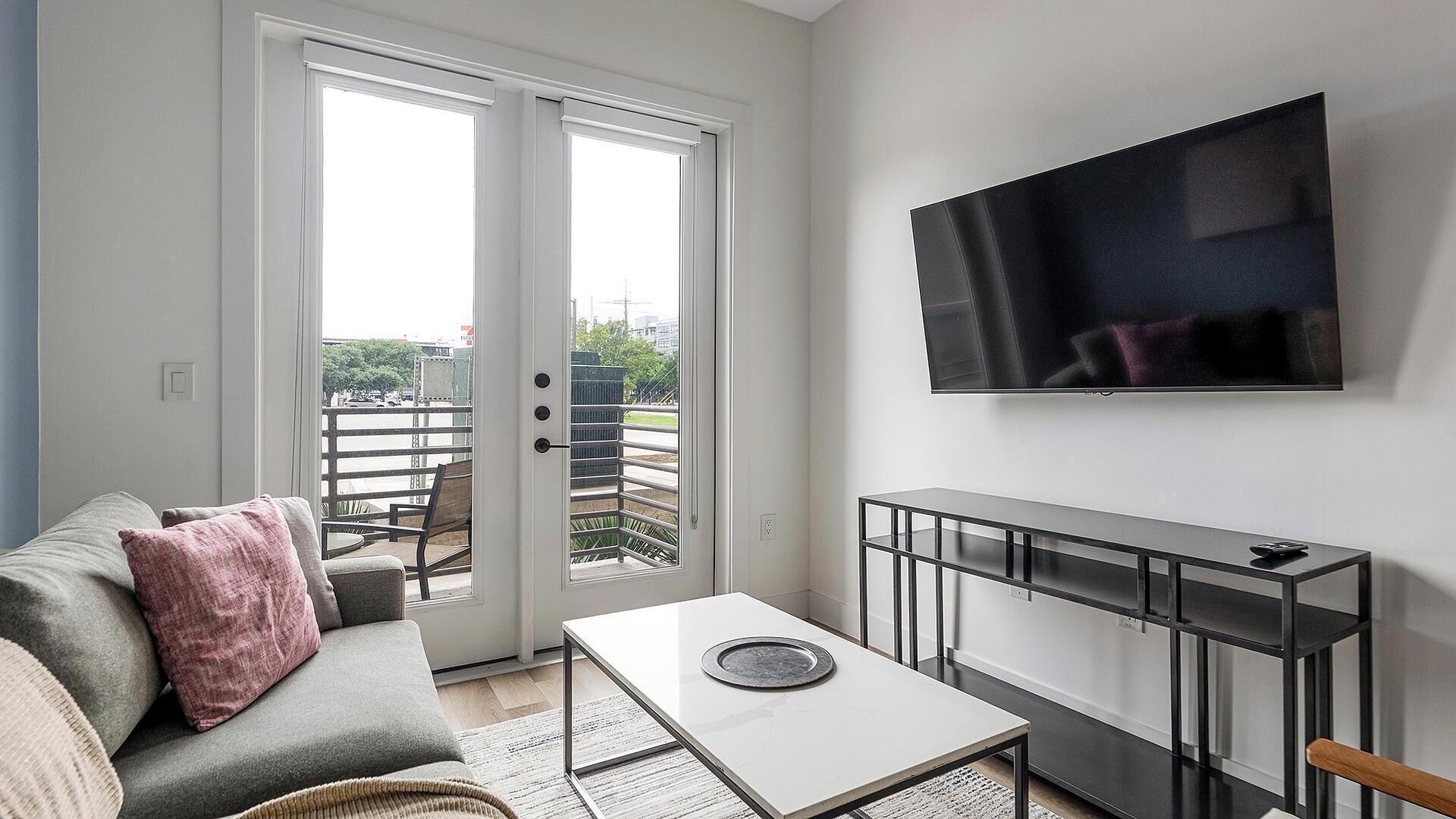A modern living room with a sofa, a coffee table, a TV mounted on the wall, and a balcony with a railing.