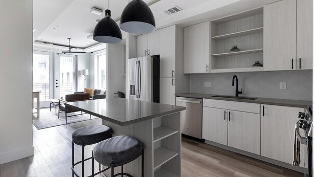 A modern kitchen with a central island, bar stools, and pendant lighting. - Landing | Modern 1BD, Gym (Austin)