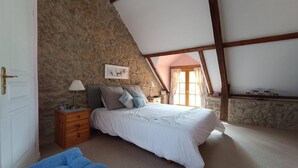 Ein Schlafzimmer mit Steinwand, einem Bett mit weißer Bettwäsche, einem Nachttisch mit Lampe und einem Fenster mit Vorhängen.