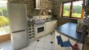 Eine Küche mit Steinwand, Kühlschrank, Herd und Fenster mit Blick auf Grünfläche.