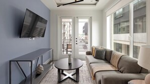 Een moderne woonkamer met een televisie, een ronde tafel, een bank en een balkon met uitzicht op de stad.