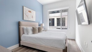 Una camera da letto con un letto, un comodino, una lampada, una finestra e una TV a parete.