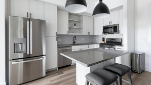 A modern kitchen with stainless steel appliances, a central island, and pendant lighting. - Landing | Spectacular 1BD, Gym (Austin)