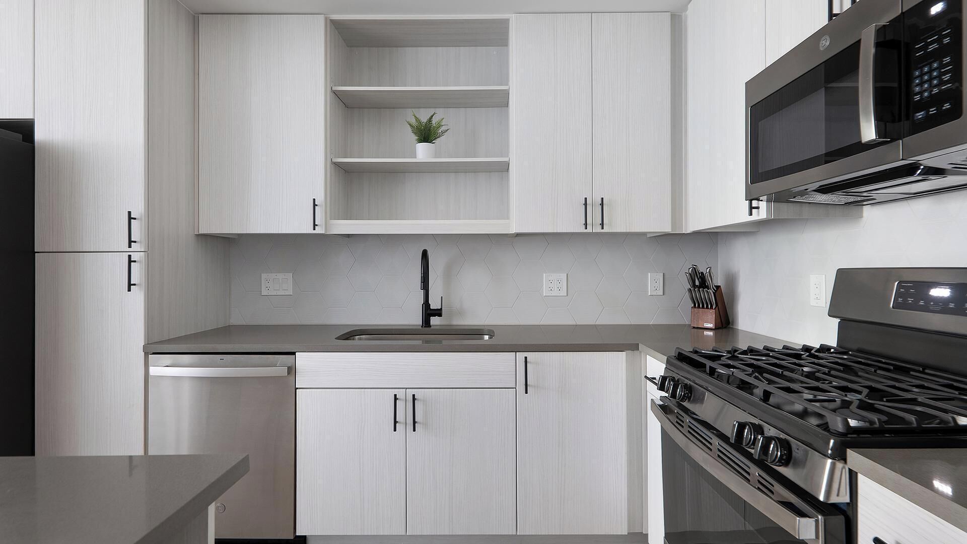 A modern kitchen with white cabinetry, a stainless steel dishwasher, a sink, a stove, and a microwave.