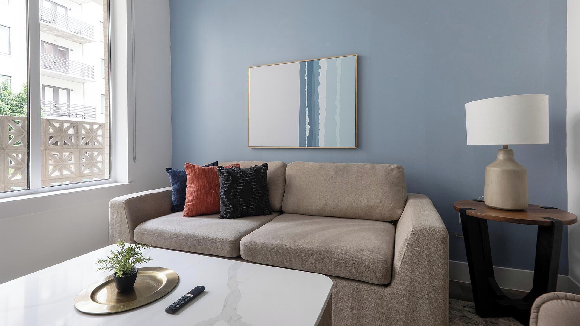 Un soggiorno moderno con un divano beige, un tavolino, una lampada e un quadro appeso al muro.