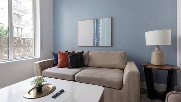 Un salon moderne avec un canapé beige, une table basse, une lampe et un tableau accroché au mur.