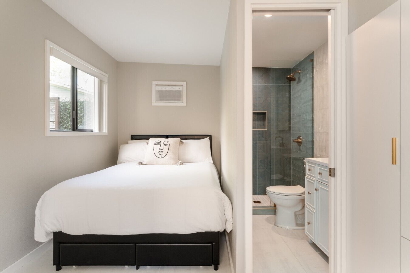 A bedroom with a bed, a window, a bathroom with a shower, and a toilet.