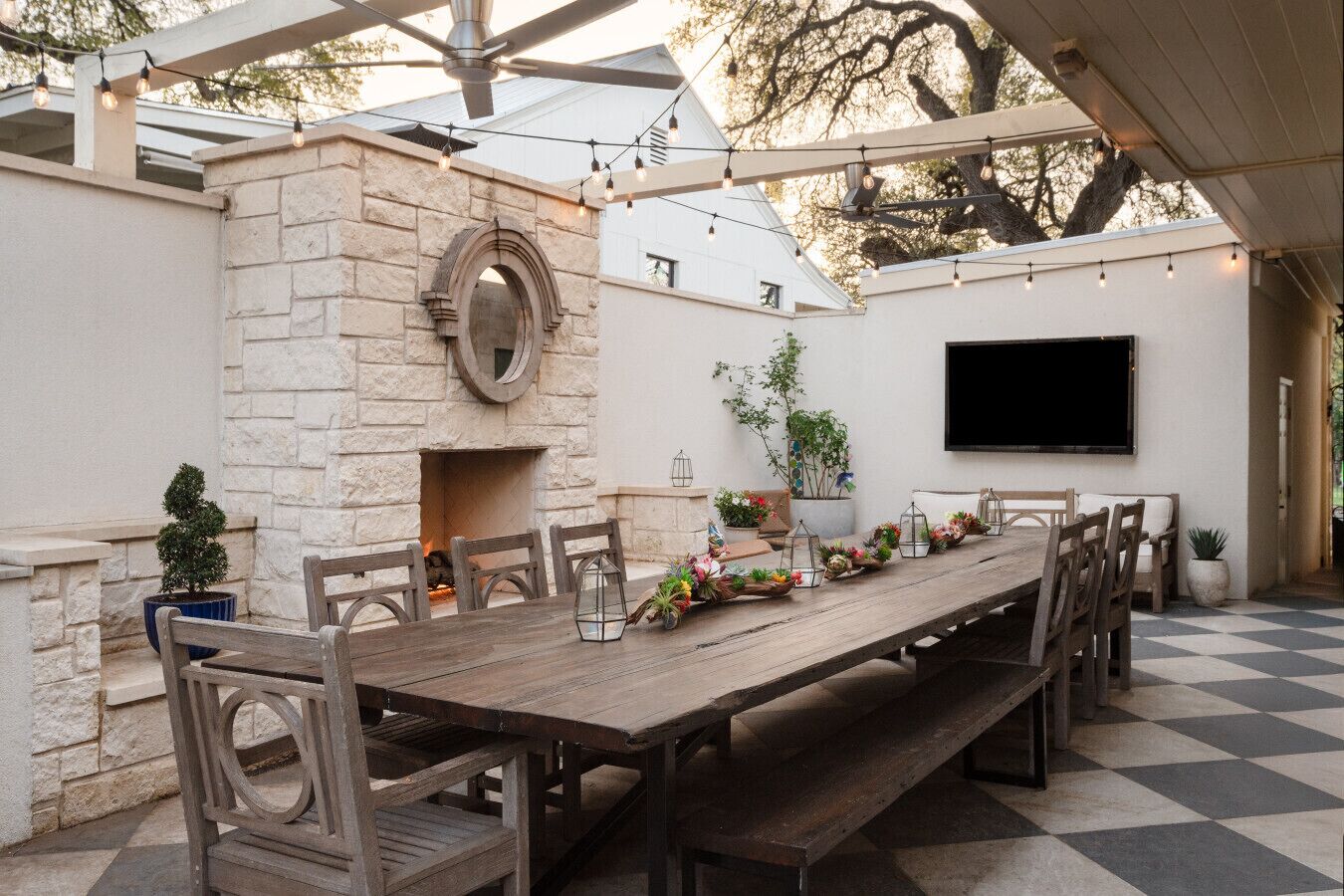 An outdoor dining area with a stone fireplace, a long wooden table, and chairs.