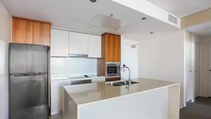 Een moderne keuken met een roestvrijstalen koelkast, houten kastjes, een magnetron en een groot kookeiland met een spoelbak.