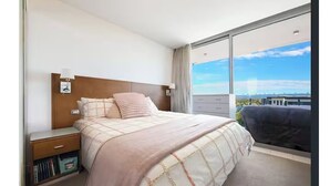 Hotelkamer met een groot bed, nachtkastje, kapstok en raam met uitzicht op de stad.