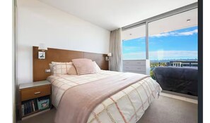 Ein Hotelzimmer mit einem großen Bett, einem Nachttisch, einer Kommode und einem Fenster mit Blick auf die Stadt.