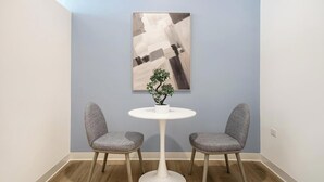 Een kamer met een ronde witte tafel, twee grijs gestoffeerde stoelen, een kleine potplant en een groot abstract schilderij aan de muur.