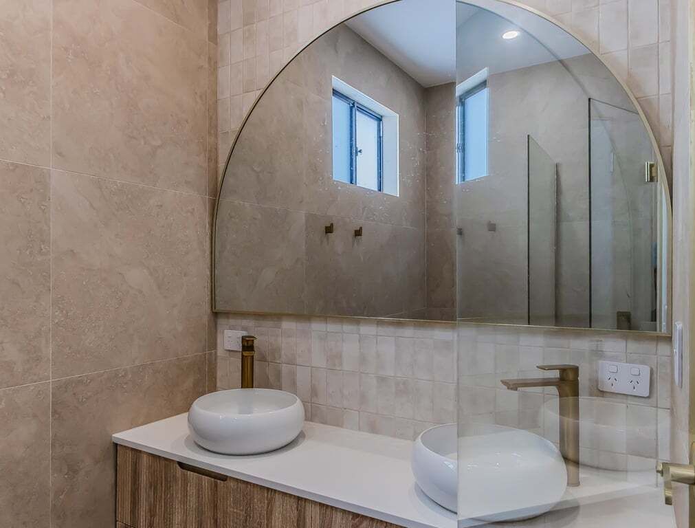 A bathroom with a round mirror, two sinks, and a shower area.