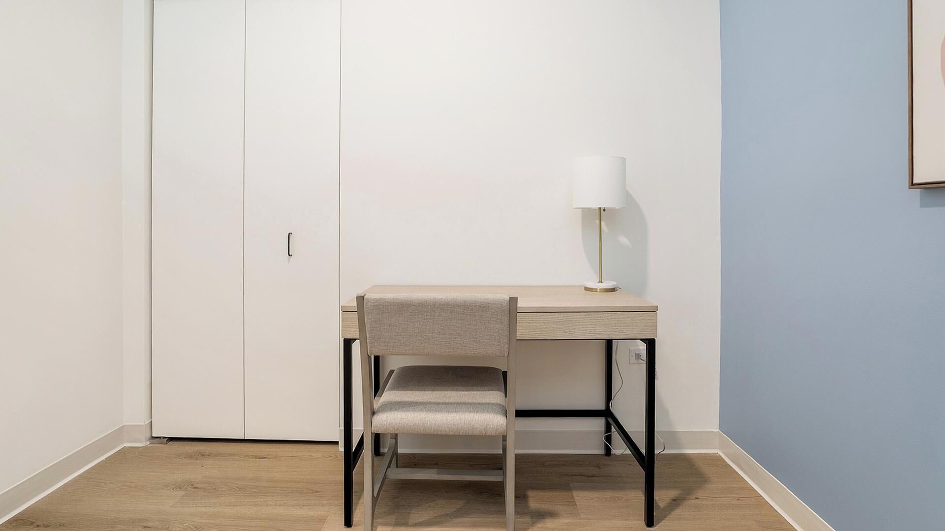 A room with a desk, chair, and lamp.