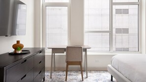A bedroom with a bed, a desk, a chair, a dresser, and a window with blinds. - Landing | Spectacular Studio in Lincoln Park (Chicago)