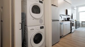 A laundry room with stacked washing machines and a modern kitchen with a dishwasher and stove. - Landing | Spectacular Studio in Lincoln Park (Chicago)