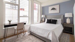 A bedroom with a large bed, two bedside tables with lamps, a chair, and a window with blinds. - Landing | Beautiful Studio in Lincoln Park (Chicago)