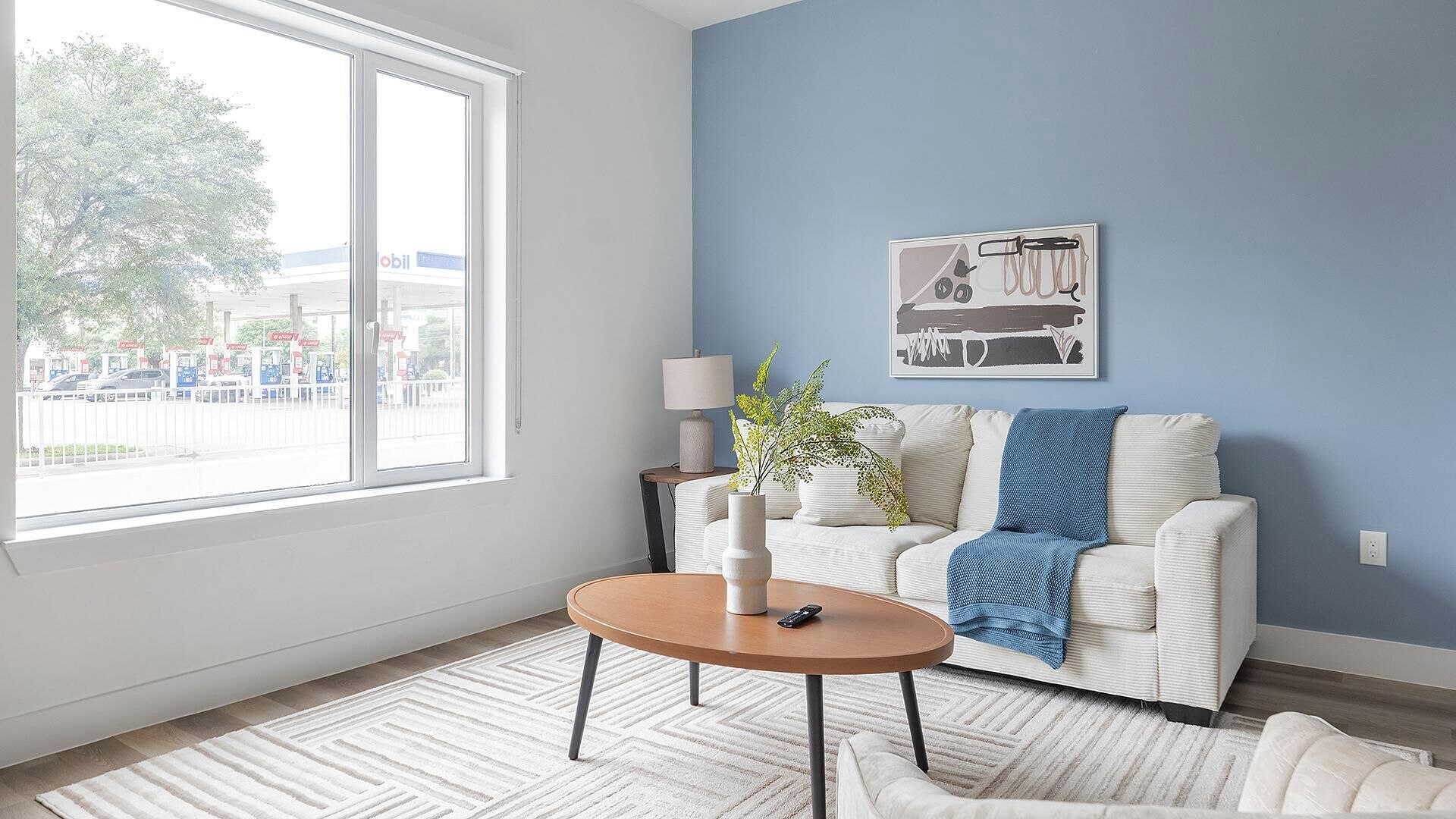 Ein Zimmer mit einem großen Fenster, einem Sofa, einem kleinen Tisch und einer Wandlampe.