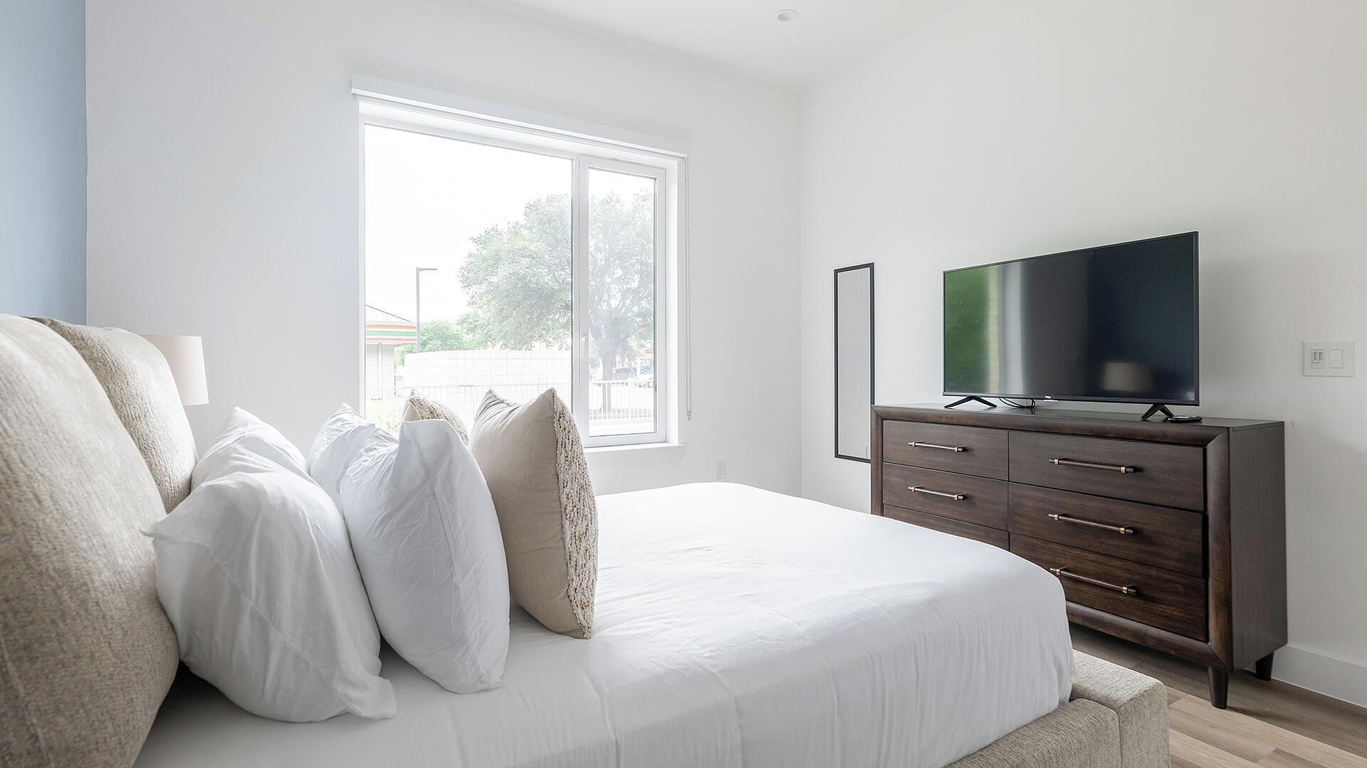 A bedroom with a bed, a dresser, a television, and a window.