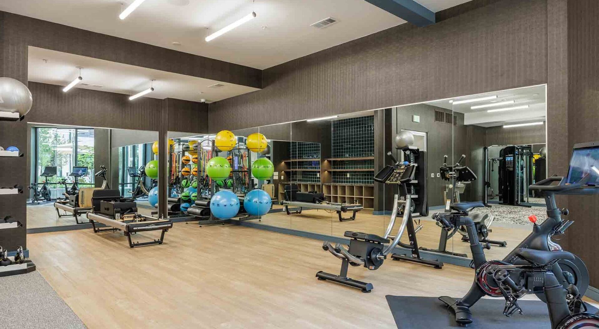 Ein Fitnessstudio mit Trainingsgeräten, Spiegeln und Holzboden.