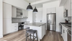 Une cuisine moderne dotée d’un îlot central, d’appareils électroménagers en acier inoxydable et de meubles de cuisine en bois clair.