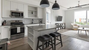 A modern kitchen with a central island, stainless steel appliances, and pendant lighting. - Landing | Stylish 1BD, Gym (Austin)