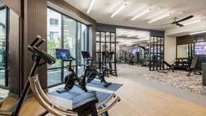 Ein modernes Fitnessstudio mit Trainingsgeräten, großen Fenstern und einem Deckenventilator.