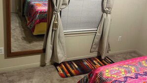 Ein Schlafzimmer mit einem Bett, einem Fenster mit Jalousien, einem Spiegel und einer Tür.