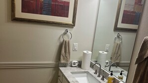 Ein Badezimmer mit Waschbecken, Spiegel, Handtuchhaltern, Toilette und einem gerahmten abstrakten Gemälde.