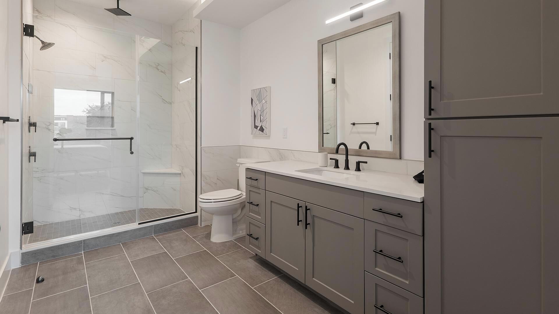 Ein modernes Badezimmer mit Duschkabine aus Glas, Toilette, Waschbecken mit Spiegel und Schränken.
