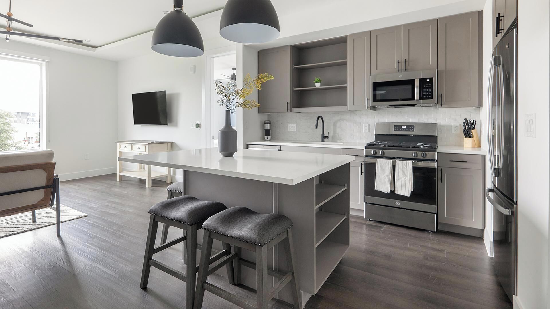 A modern kitchen with a central island, bar stools, stainless steel appliances, and a flat-screen TV.