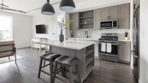 Uma cozinha moderna com uma ilha central, banquetas, eletrodomésticos de aço inoxidável e uma TV de tela plana.