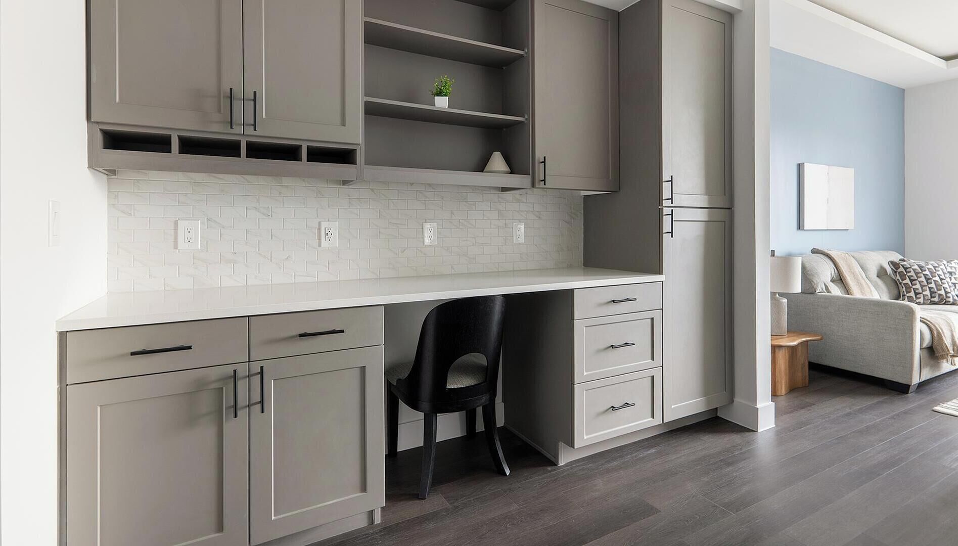 A modern kitchen with grey cabinetry, a white countertop, and a black chair.