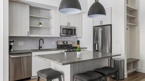 Een moderne keuken met roestvrijstalen apparatuur, een centraal eiland met barstoelen en hanglampen.