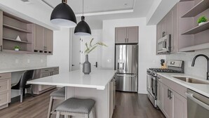 Una cocina moderna con una isla central, electrodomésticos de acero inoxidable, iluminación colgante y un diseño minimalista.