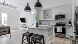 Une cuisine moderne dotée d’un îlot central, d’appareils électroménagers en acier inoxydable et de luminaires suspendus.