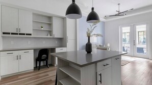 Une cuisine moderne avec des meubles blancs, un îlot central, des luminaires suspendus et une vue sur l’extérieur.
